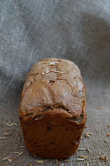 A whole loaf of homemade pastries with oat and wheat seeds on a background of rough burlap.