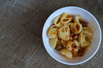 Seashell pasta with meat sauce in a white bowl on a background of rough burlap