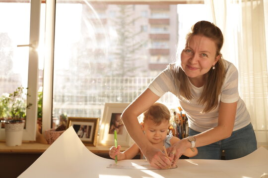 Beautiful woman cutting dress patterns in home with her little cute girl