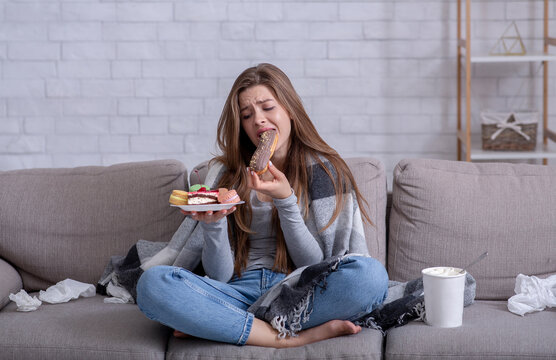 Comfort foods and stress eating concept. Frustrated young lady devouring pastry on sofa at home