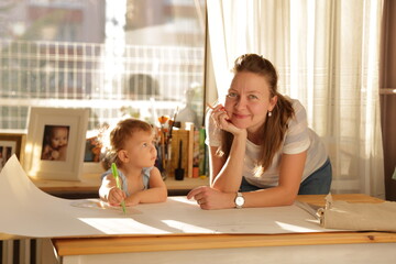 Beautiful woman cutting dress patterns in home with her little cute girl