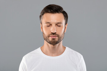 Middle-aged man with closed eyes over grey studio background
