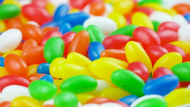 Multicolor Jelly Beans Candy Fall Down on Rotating Background. Bright Tasty Colourful Texture Of Blue, Green, Yellow, Red, Orange and White Sweets on Turn Table