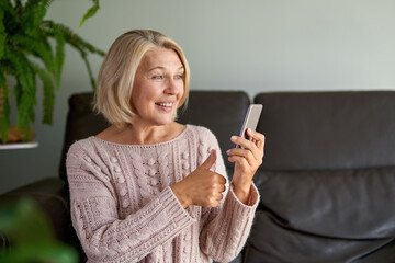 Happy senior woman using phone call sitting on a sofa in the living room in a house