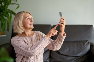 Happy senior woman using phone call sitting on a sofa in the living room in a house