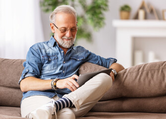 Fototapeta premium Cheerful aged man using tablet on couch.