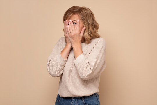 Cheerful mature caucasian woman covering her face using hands looking through fingers