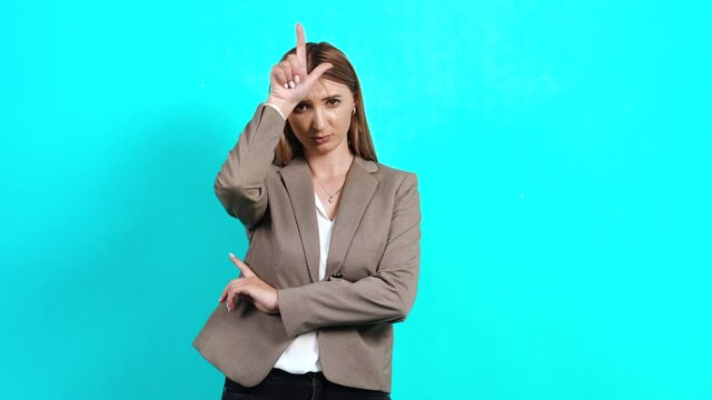 Upset young woman disappointed in business jacket, keeping her fingers near her forehead, showing the sign of lost sarcasm, unhappy because of the crisis. Studio image indoors, isolated on blue