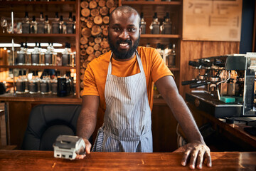 Cheerful male barman holding terminal for contactless payment