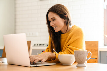Beautiful woman using laptop computer while having breakfast at home
