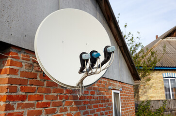 Satellite dish is attached to the wall of the house. A domestic satellite tv installation under roof