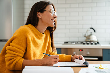 Beautiful caucasian woman smiling and working with papers in apartment