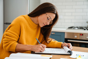 Beautiful caucasian woman smiling and working with papers in apartment