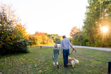 Father and daughter walking dog outdoors on autumn day