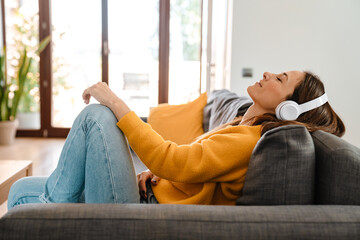 Happy woman listening to music in headphones on sofa at home