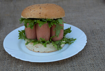 A sandwich with salad and sausage lies on a jute fabric on a white plate.