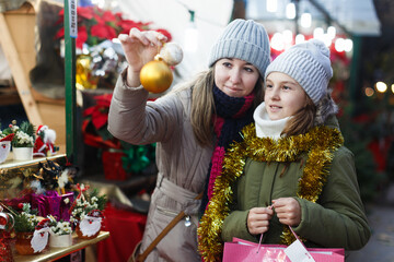Woman and her daughter are preparing for Christmas and choosing balls on the tree outdoor.