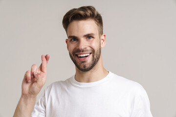 Joyful handsome guy posing with fingers crossed for good luck