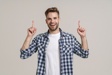 Joyful handsome unshaven guy smiling and pointing fingers upward