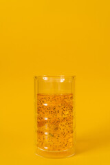 A glass of mango drink with basil seeds on a yellow background.