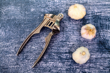 Three garlic bulbs and a press on a textured background