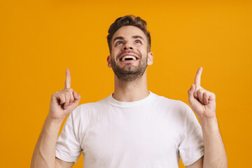 Joyful handsome unshaven guy smiling and pointing fingers upward