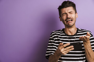 Photo of unhappy man crying while playing video game on cellphone