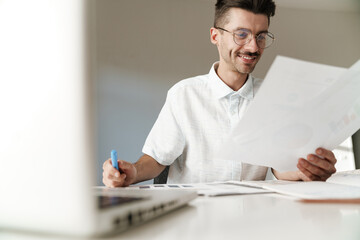 Photo of smiling unshaven man working with laptop and papers at table