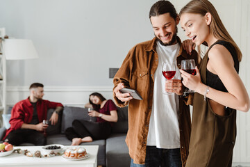 Image of multinational friends using mobile phone while drinking wine