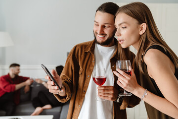 Image of multinational friends using mobile phone while drinking wine