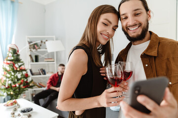 Image of friends taking selfie on mobile phone while drinking wine