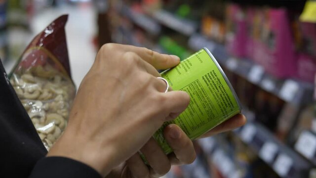 Close up of two hands holding canned product to read ingredients details in store. Conscious shopping concept