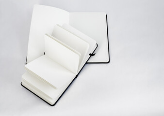 Large and small black open new notebooks with blank white pages and dark ribbons bookmarks lie unfold on a white background