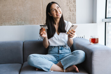 Obraz premium Smiling young woman in casual clothes sitting on couch