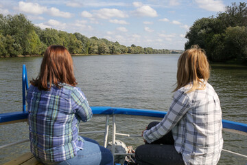 Fototapeta premium Two women sit back on bow of yacht and look at the river. Lesbians ride on a riverboat.