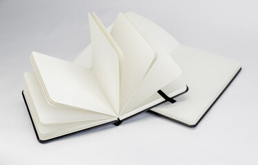 Two black new notebooks with blank white pages and dark ribbons bookmarks lie unfold on a white background
