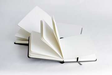Black open small notepad and unfold large notebook with blank light beige pages. White background.