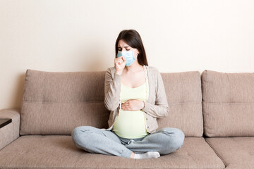 Pregnant woman in protection mask sitting on sofa. COVID-19 Coronavirus. Prevent infection to the fetus