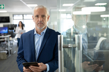 Portrait of senior businessman holding digital tablet at modern office