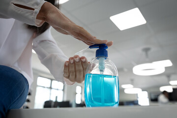 Mid section of businesswoman sanitizing her hands at office