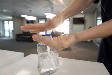 Mid section of businesswoman sanitizing her hands at office