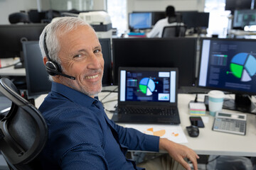 Portrait of senior businessman wearing headset sitting on his desk at modern office