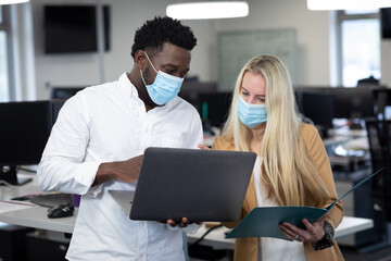 Businessman and businesswoman wearing face masks working together at modern office