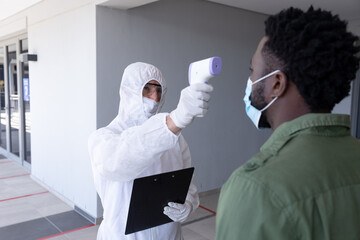 Health worker wearing protective clothes checking temperature of businessman