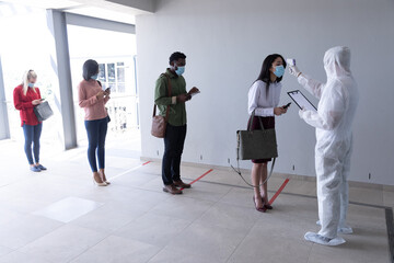 Health worker wearing protective clothes checking temperature of businesswoman