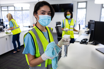 Fototapeta na wymiar Portrait of woman wearing hi vis vest and face mask holding cleaning cloth and disinfectant