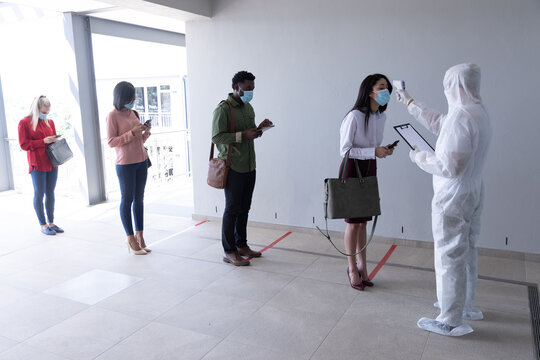 Health worker wearing protective clothes checking temperature of businesswoman