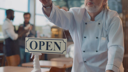 Chef cleaning window and turning open sign board on glass door in modern cafe
