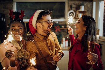 Fototapeta premium Cheerful young adults drinking champagne and using sparklers on New Year's party at home.
