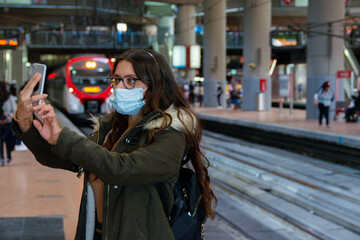 Mujer haciendo un autofoto con mascarilla en una estación de tren en Madrid